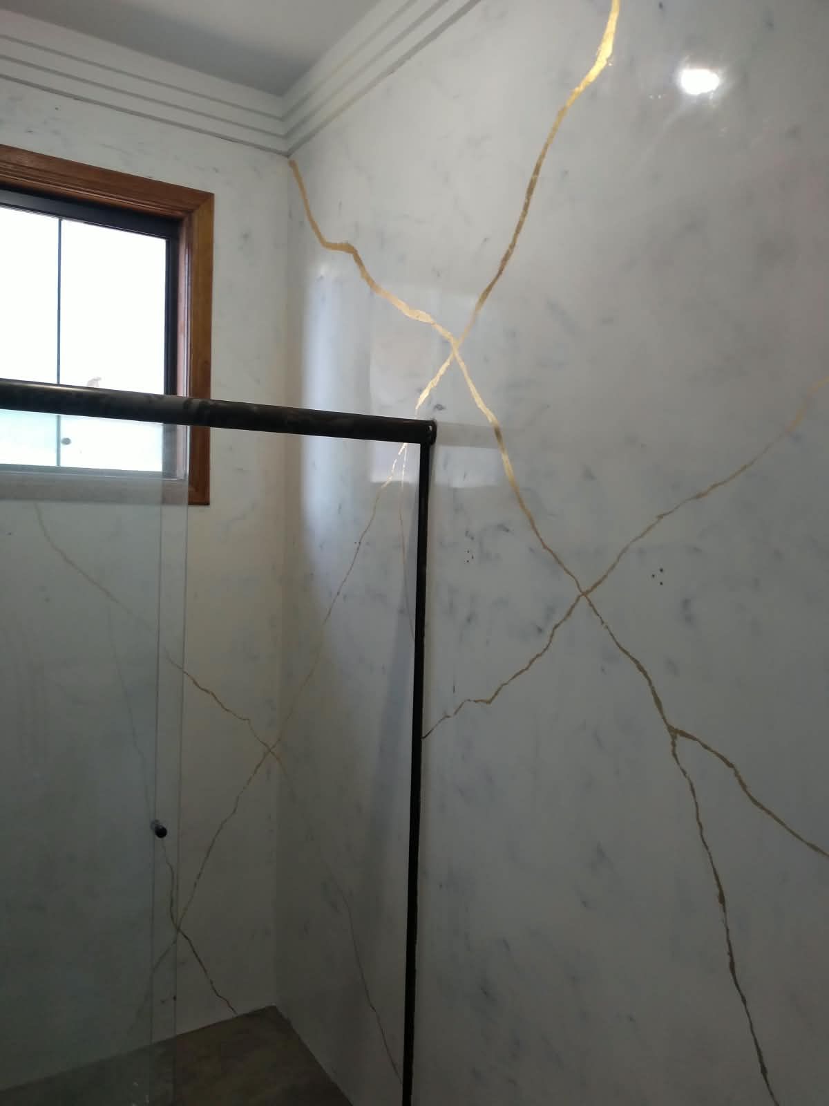 Parede de banheiro em marmorato branco com veio dourado marcado, ao lado de janela de madeira